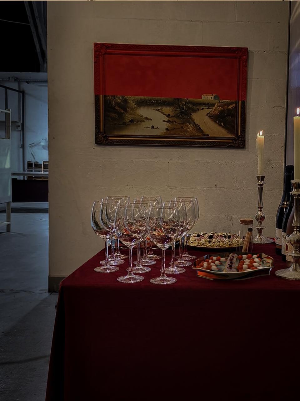 Wine glasses poured and waiting in rows on a red tablecloth, candles beside them, before the first guests arrive.