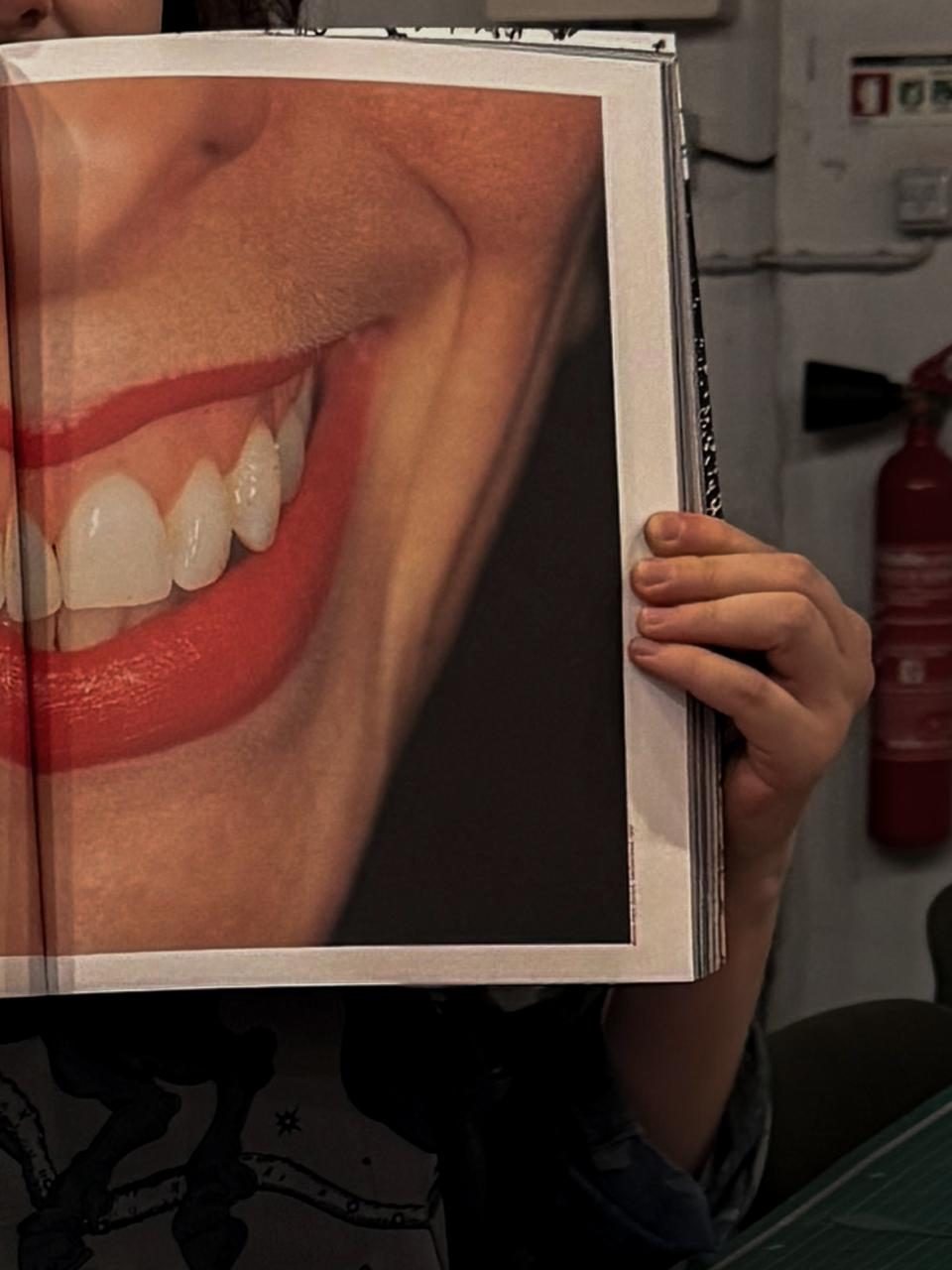 A guest holding an open magazine spread up in front of their face — a close-up of a smile printed across the page.