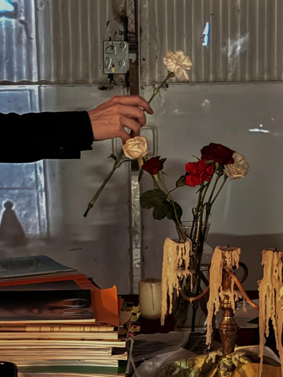 An arm reaching past the candlesticks to place a carnation, above stacks of catalogues.
